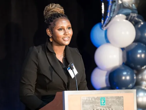 Une femme prend la parole à la tribune lors d'un événement de remise de bourses d'études de l'AEF, dans un hôtel Embassy Suites à Washington, DC, décoré de ballons bleus et blancs.