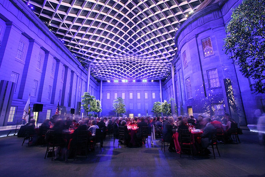 participantes sentados em um evento no Pátio Kogod iluminado à noite com uma arquitetura grandiosa