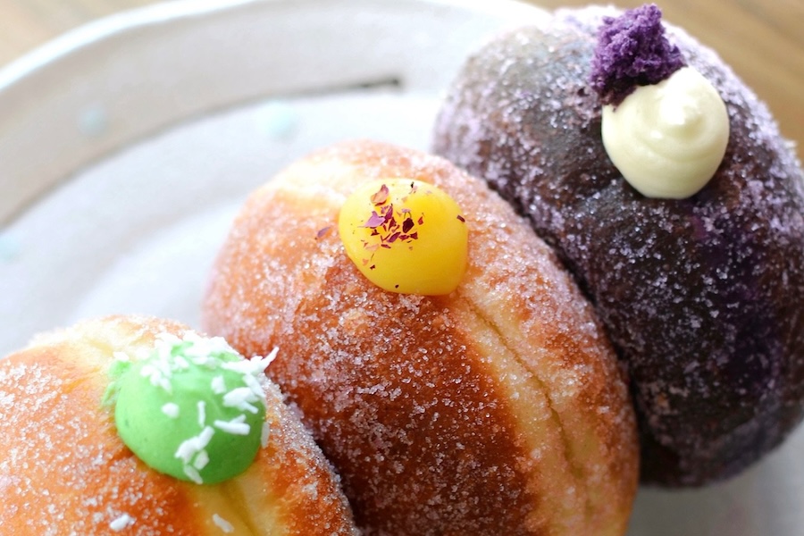 um trio de donuts de brioche recheados com ube, maracujá e pandan em um prato