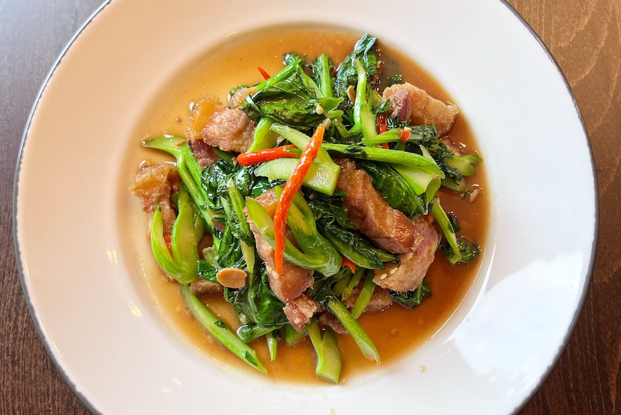 thai dish with bright greens and a bright red chile on a wooden table