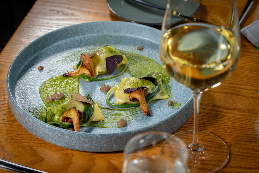 Gravitas: slanted angle view of dish with green sauce on blue plate with glass of wine and wood table
