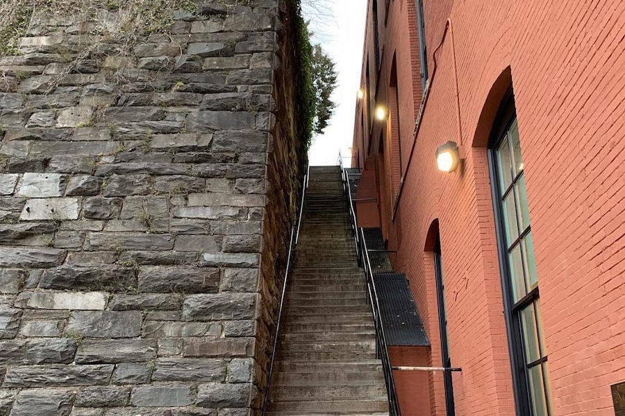 石墙和红砖建筑之间的陡峭楼梯，建筑上安装的灯照亮了台阶。