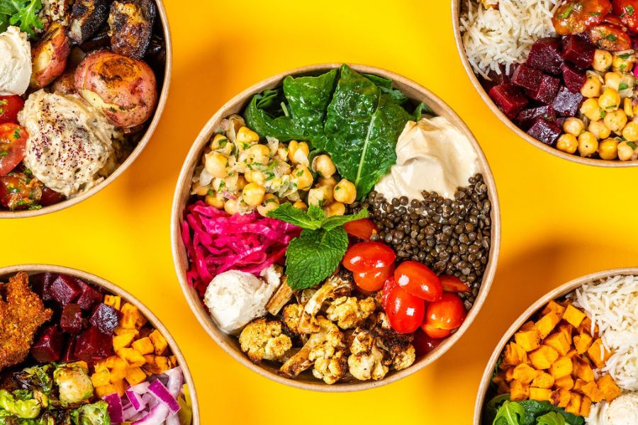 This image features a variety of colorful bowls filled with fresh ingredients such as roasted vegetables, grains, chickpeas, lentils, greens, and sauces. The bowls are arranged on a bright yellow background, emphasizing the vibrant and healthy presentation.