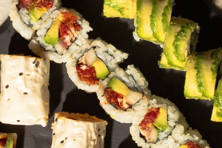 This image showcases an assortment of vegan sushi rolls, featuring ingredients like avocado and various fillings wrapped in rice and seaweed. The rolls are neatly arranged on a dark surface, highlighting their vibrant colors and fresh appearance.