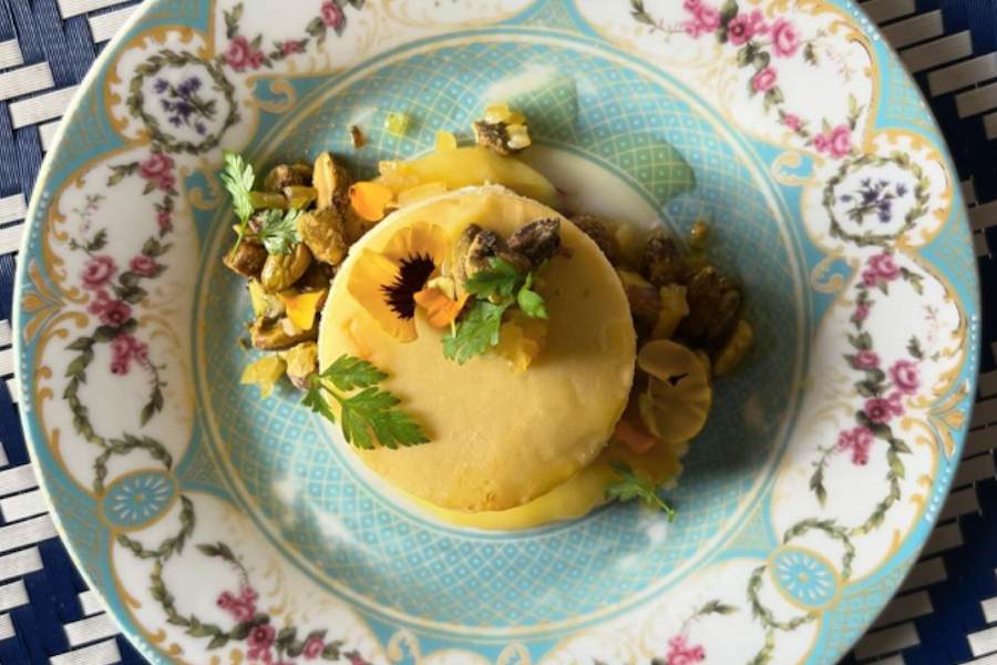 Close-up of a beautifully plated cheesecake with pistachios and edible flowers on an ornate blue and white dish