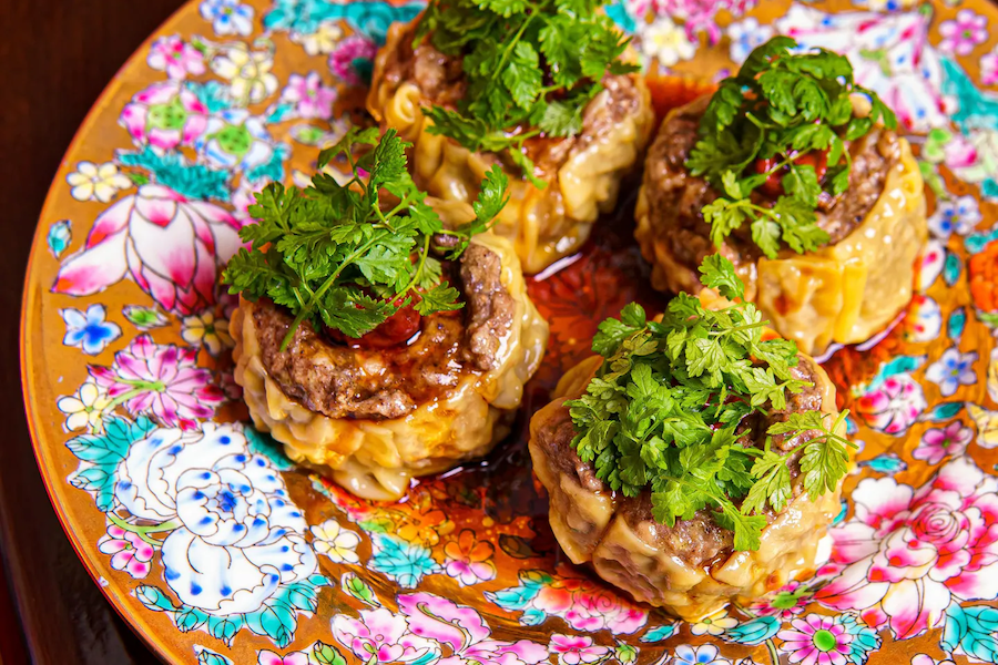 Close-up of dumplings garnished with fresh herbs, served on a vibrant, floral-patterned plate.