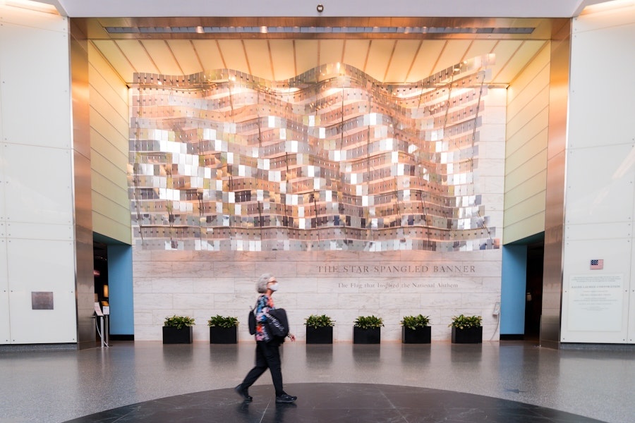 A person walks in front of a wavy, metallic sculpture titled "The Star-Spangled Banner" at the National Museum of American History.