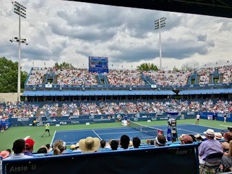 Tennis match in progress at the Citi Open with a crowd of spectators in the stands at the venue in Washington, DC.