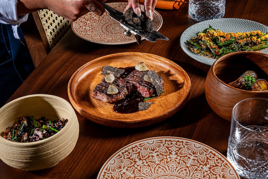 A variety of dishes served at Hiraya restaurant, including a steak with truffles, green vegetables, and other sides.