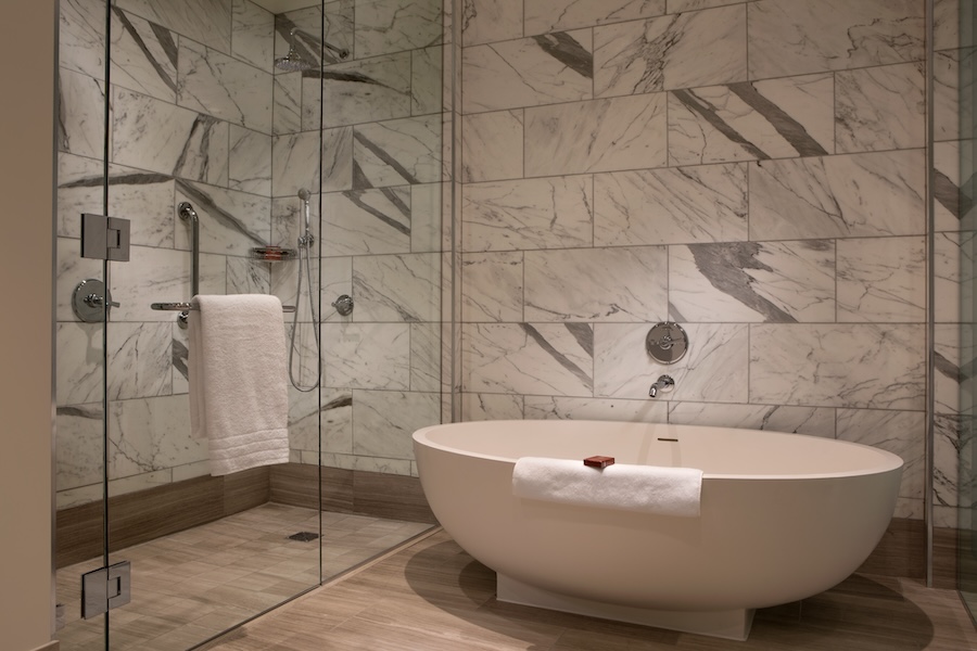 A sleek and modern marble bathroom featuring a freestanding bathtub, a glass-enclosed shower, and elegant fixtures.