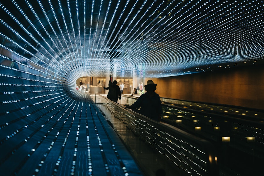 An illuminated walkway tunnel with a dynamic light display, creating an immersive and futuristic experience as visitors move through.