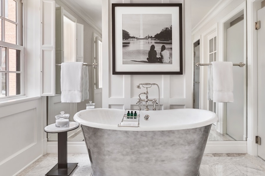 Elegant bathroom with a freestanding silver bathtub, flanked by white towels on racks, with a black and white photo of the Washington Monument above.