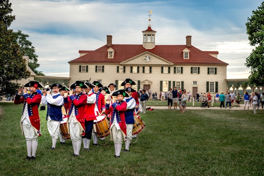 A scenic view of people in historic costumes playing instruments in front of the Mount Vernon estate.