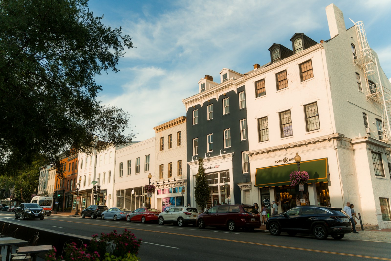 A picturesque Georgetown streetscape featuring charming historic buildings with boutique shops and parked cars, bathed in late afternoon sunlight under a clear sky.