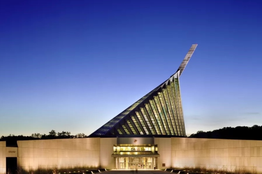 A modern architectural shot of the National Museum of the Marine Corps, showcasing its distinctive glass and steel design against a clear blue sky.