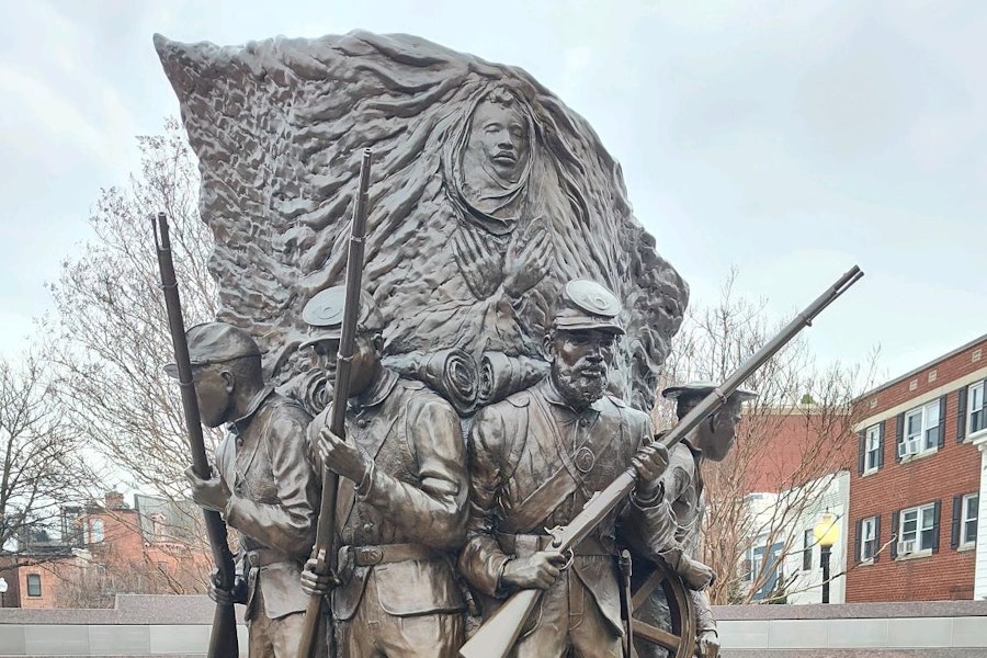 A close-up of a detailed bronze statue depicting soldiers, with a figure in the background.