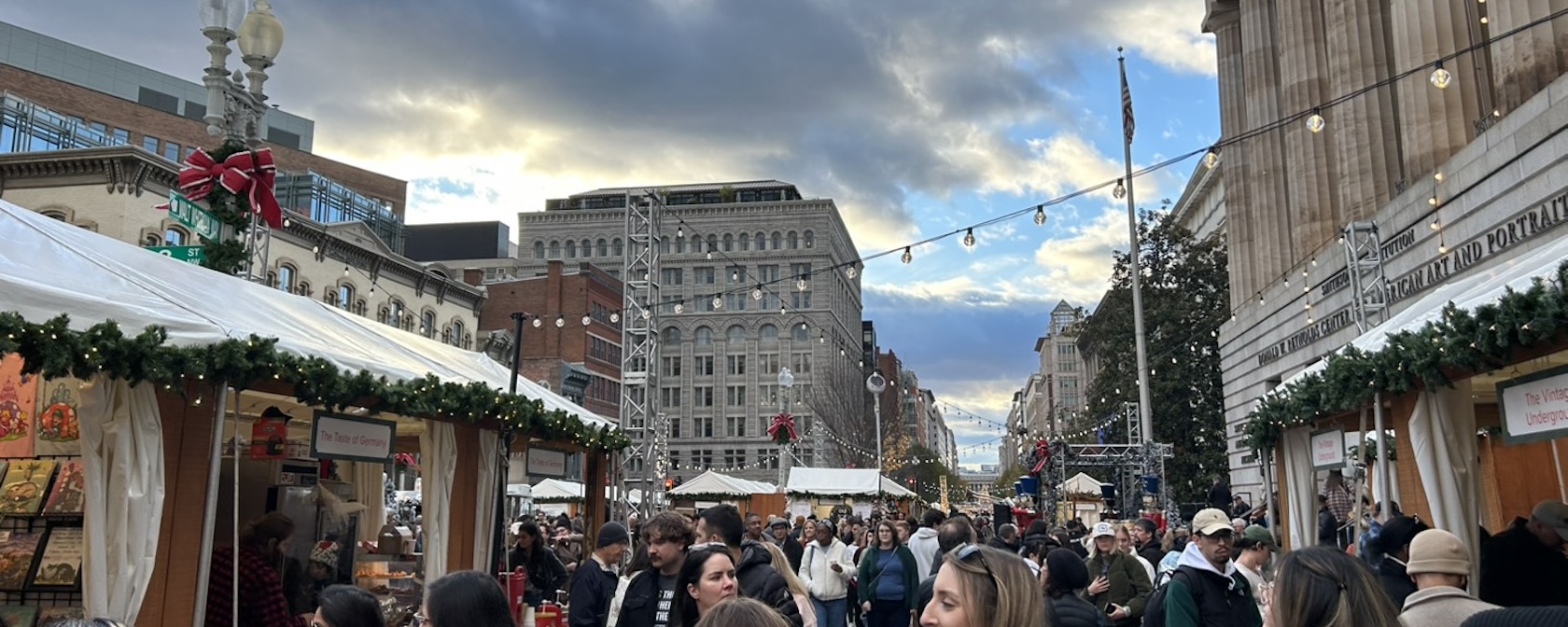 Holiday market scene in Downtown DC with crowds, festive decorations, and string lights.