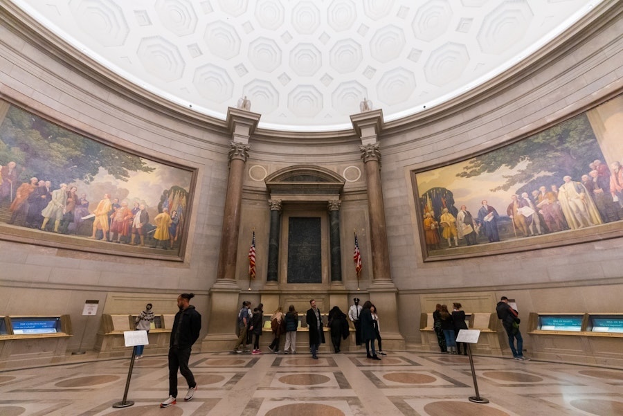 Visitors explore the Rotunda for the Charters of Freedom at the National Archives in Washington, DC, surrounded by murals and historical displays.