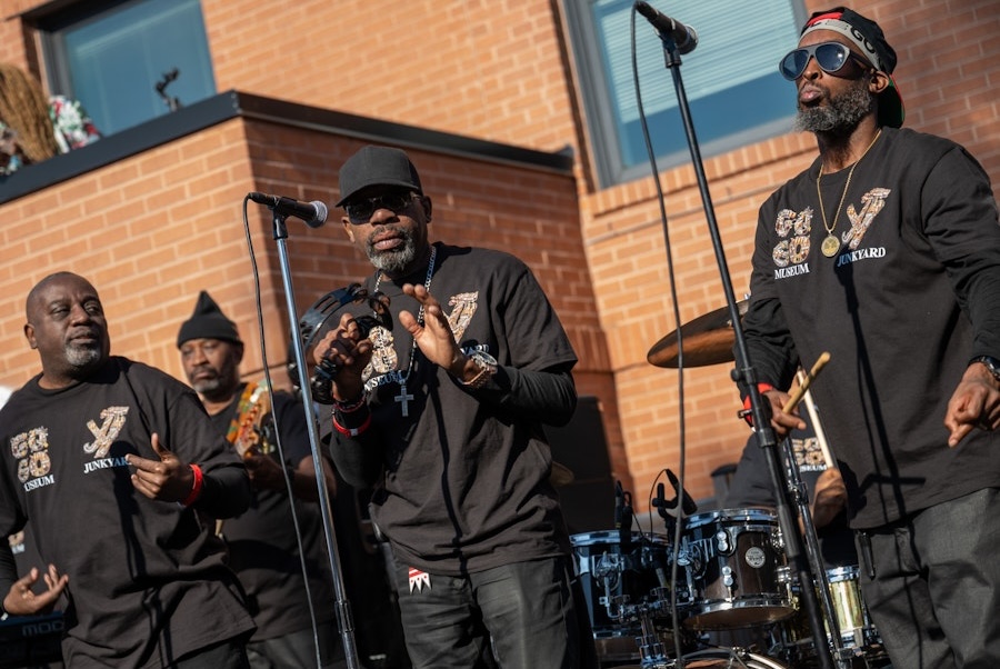 A go-go band performs outdoors, with musicians in matching black shirts engaging the crowd.