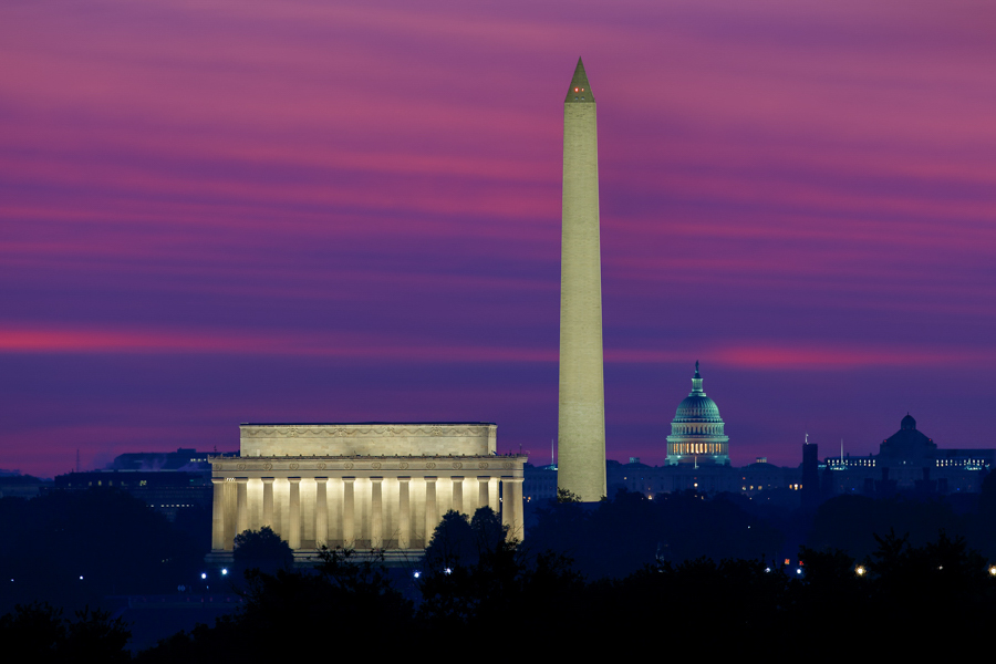 The Lincoln Memorial, Washington Monument, and U.S. Capitol glow against a deep purple and pink sunset sky.