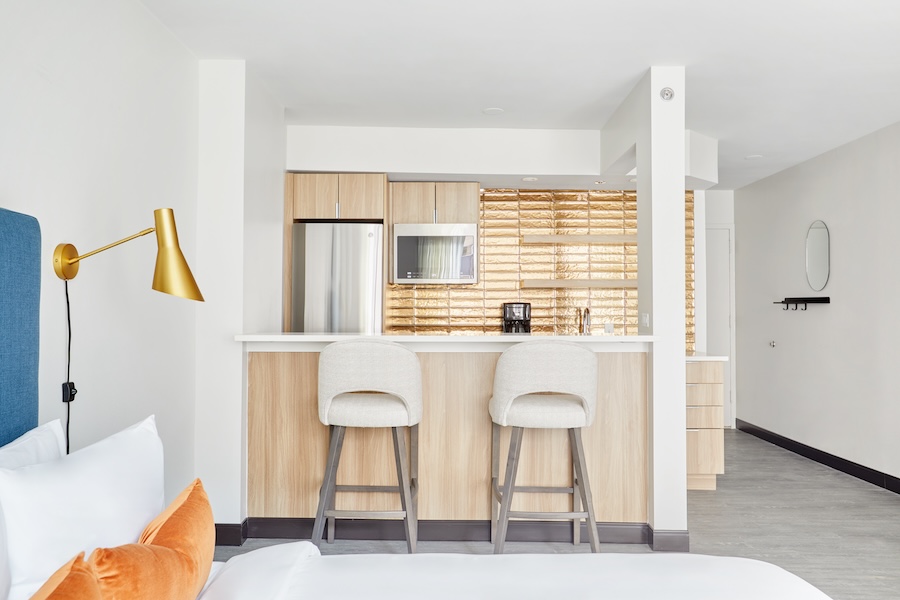 A bright, stylish hotel suite with a kitchenette and cozy seating area.