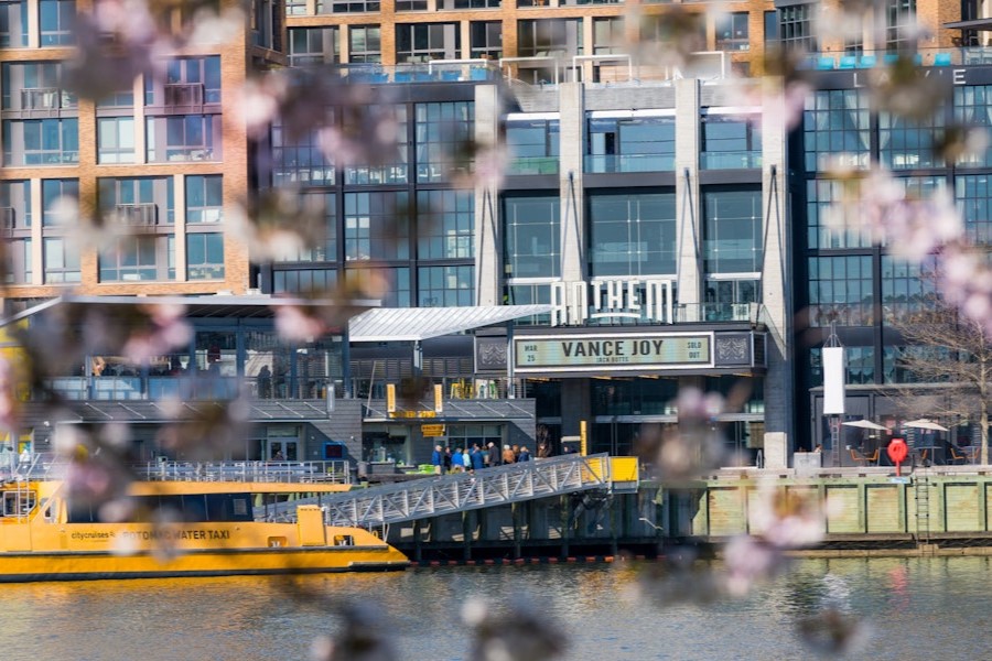 Cherry blossoms frame a view of The Anthem and a water taxi docked at The Wharf in Washington, D.C.