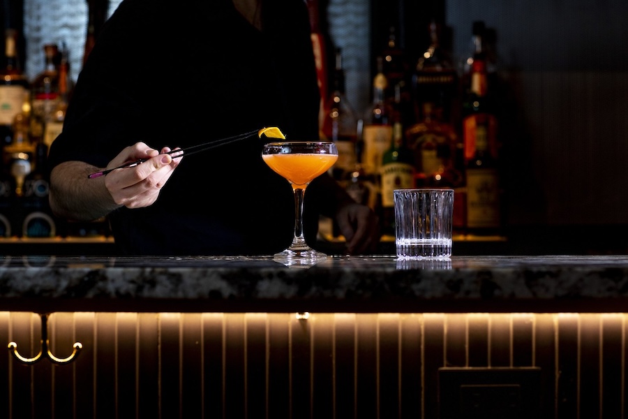 A bartender carefully garnishes a craft cocktail in a dimly lit, upscale bar.