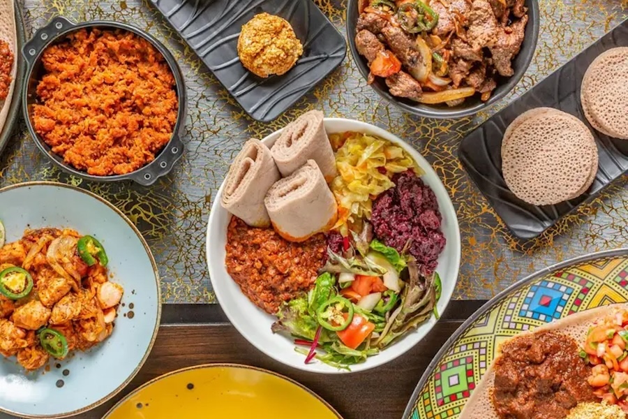 A colorful spread of Ethiopian dishes featuring injera, stews and fresh vegetables.