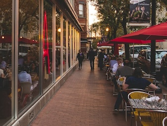 The exterior of Jaleo by José Andrés in Washington, DC, with large red neon lettering and outdoor seating under red umbrellas.