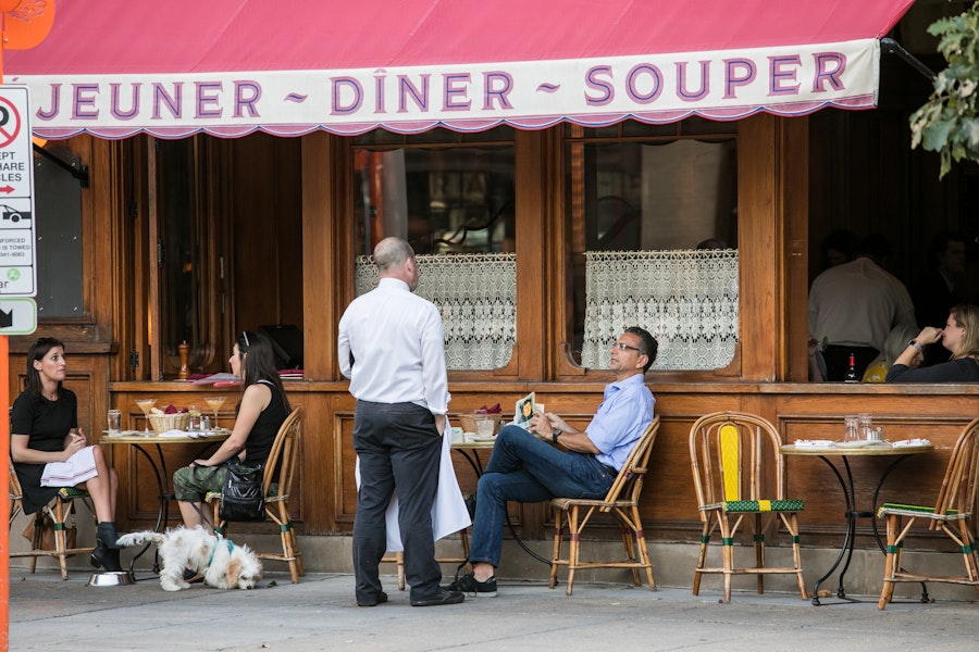 Gäste entspannen sich bei Getränken und Mahlzeiten in einem französischen Straßencafé mit Spitzenvorhängen und rosa Markise in einer Straße in Washington, D.C.