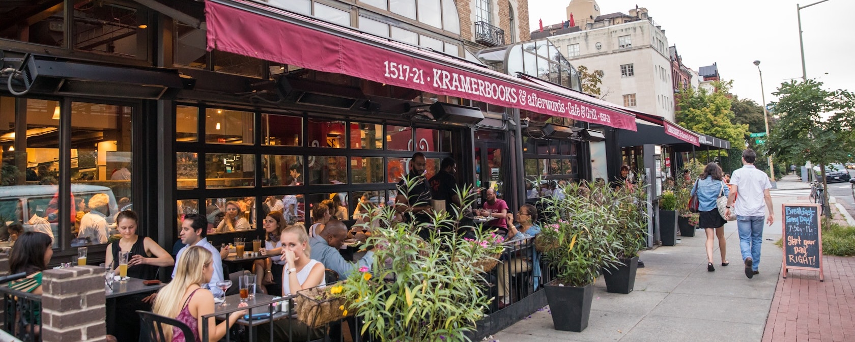 Diners enjoy outdoor seating at Kramerbooks & Afterwords Café in Dupont Circle as pedestrians stroll past the bustling sidewalk café.