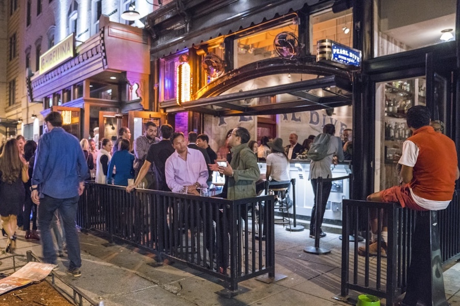 Abends versammelt sich eine lebhafte Menschenmenge vor dem Pearl Dive Oyster Palace in der 14th Street mit Sitzplätzen an der Bar im Freien und leuchtender Beleuchtung.