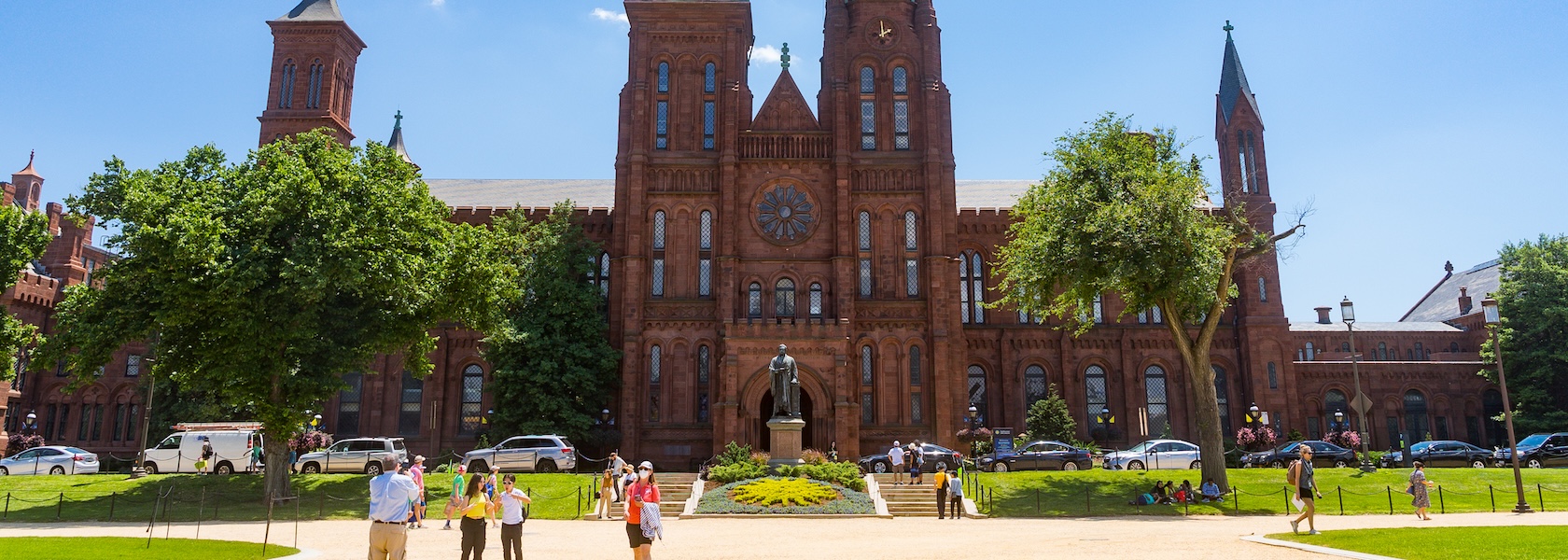 Visitors stroll across the sunny lawn in front of the iconic red sandstone Smithsonian Castle on the National Mall.