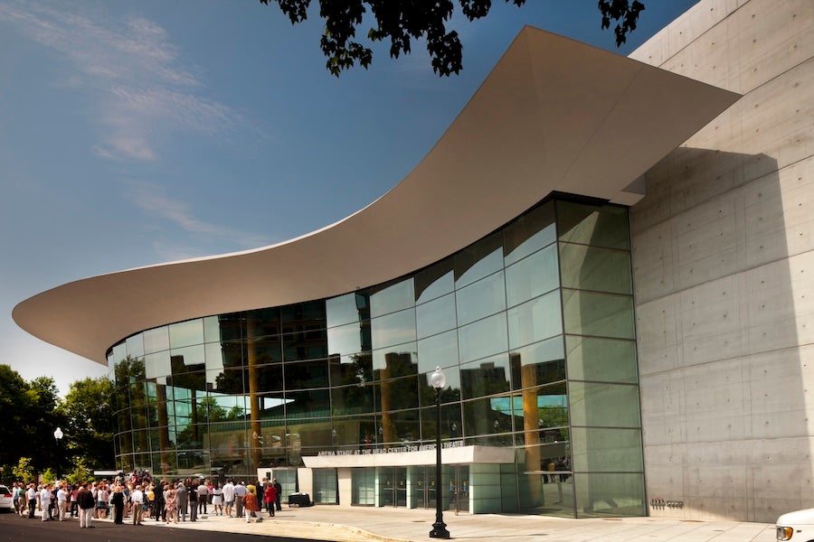 A crowd gathers outside the Arena Stage at the Mead Center under its dramatic curved roof.