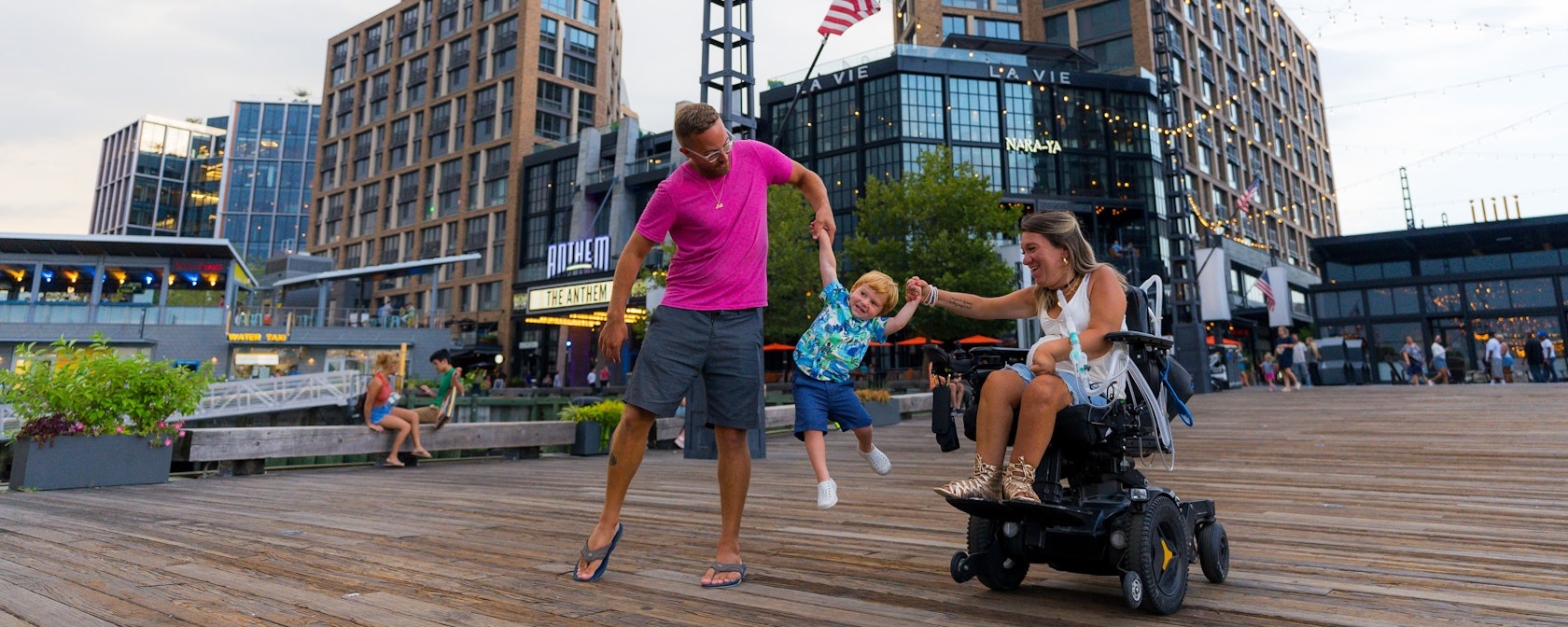 Parents hold their child's hands and swing him in the air as they enjoy a day on the Wharf. 