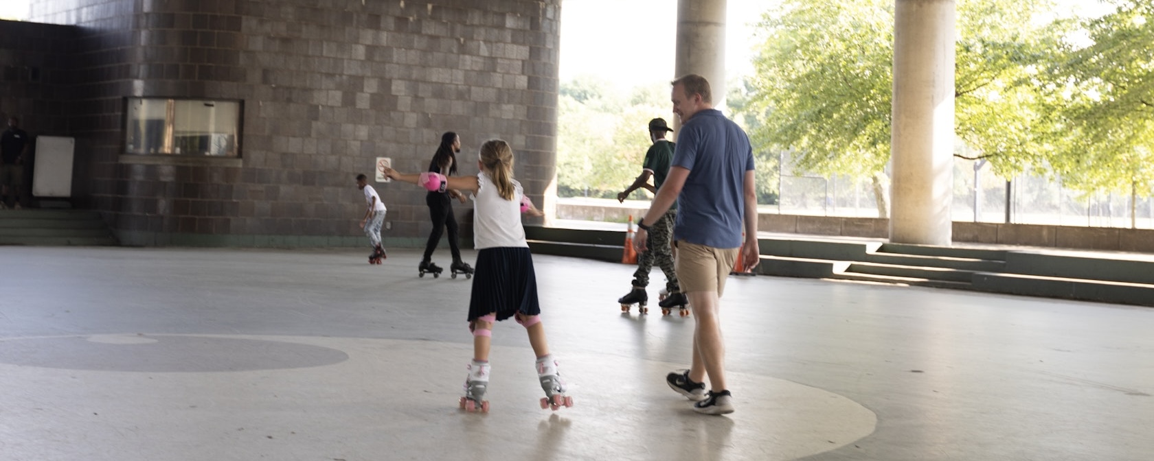 A father walks beside his daughter while she rollerblades.