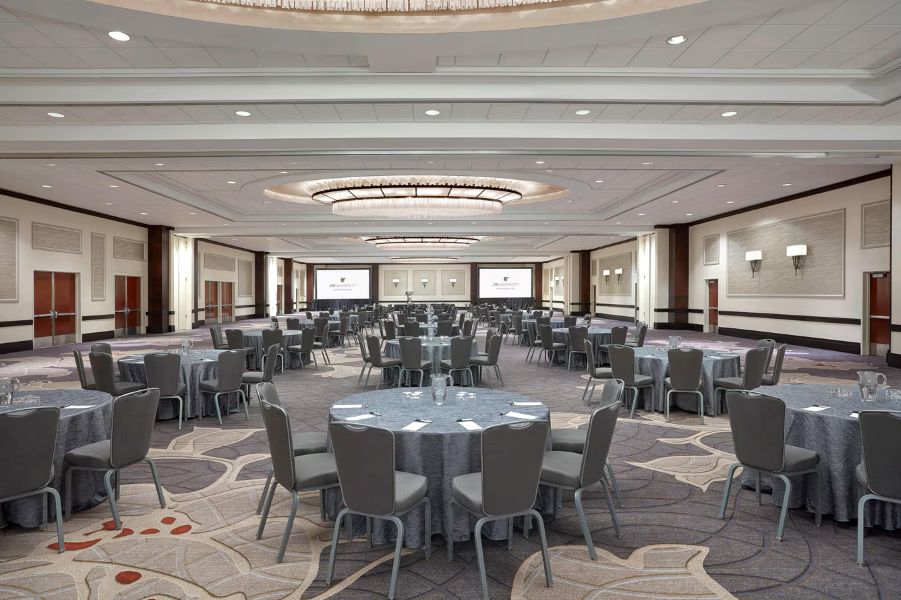 An elegant ballroom set for a formal dinner, featuring chandeliers, star-shaped light projections, round tables with pink linens, and floral centerpieces.