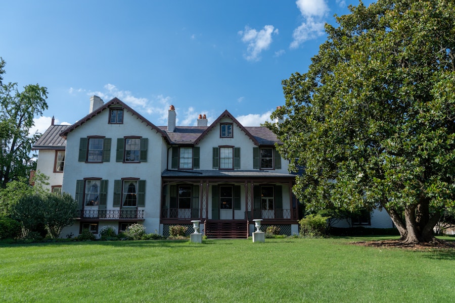 The front view of Lincoln’s Cottage shows a historic white house with green shutters surrounded by trees and an open lawn.