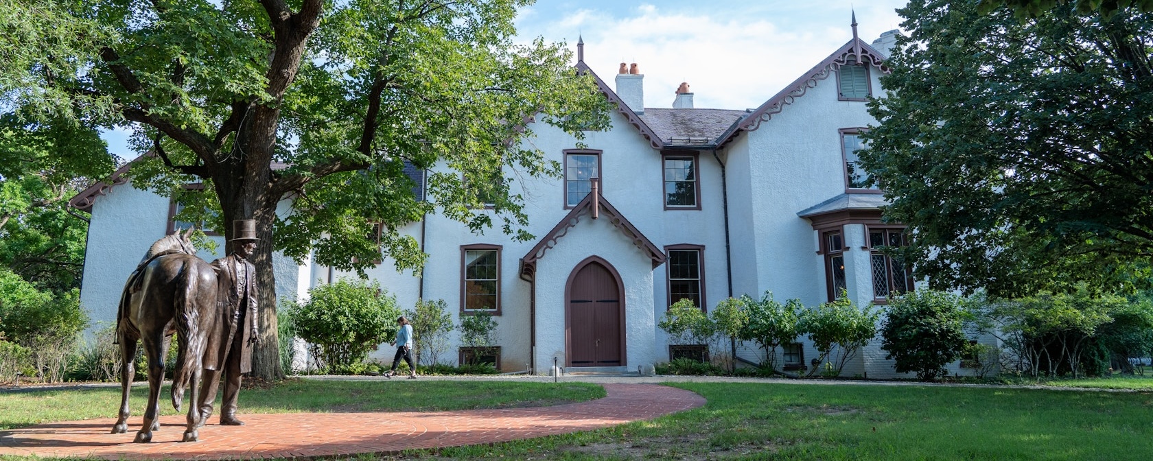 A statue of Abraham Lincoln with his horse stands before the historic Lincoln’s Cottage, surrounded by trees and greenery.