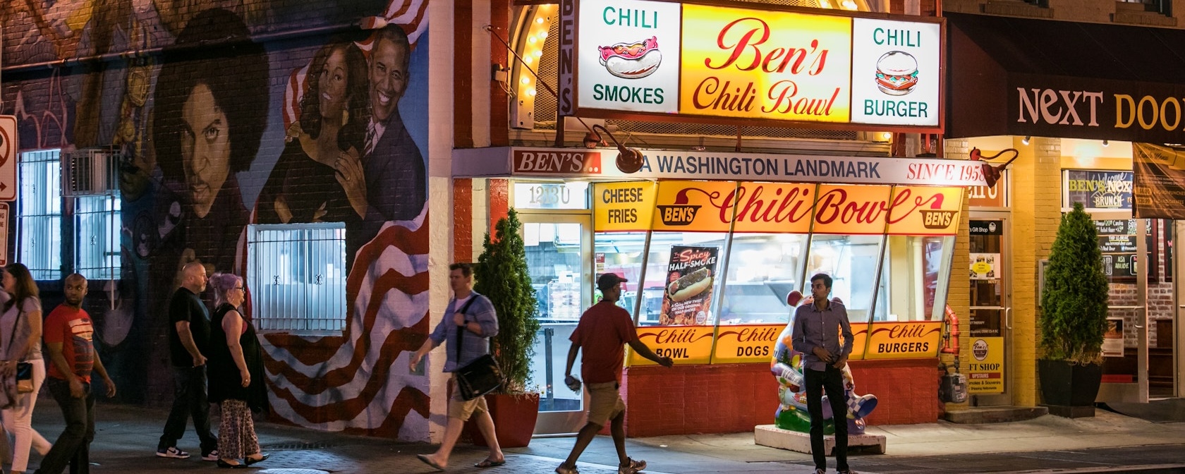 People walk by Ben's Chili Bowl at night.