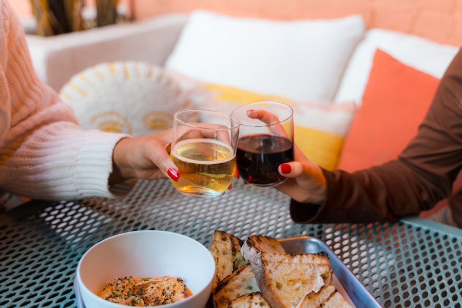 Two people clink their wine glasses together at a stylish outdoor wine garden.