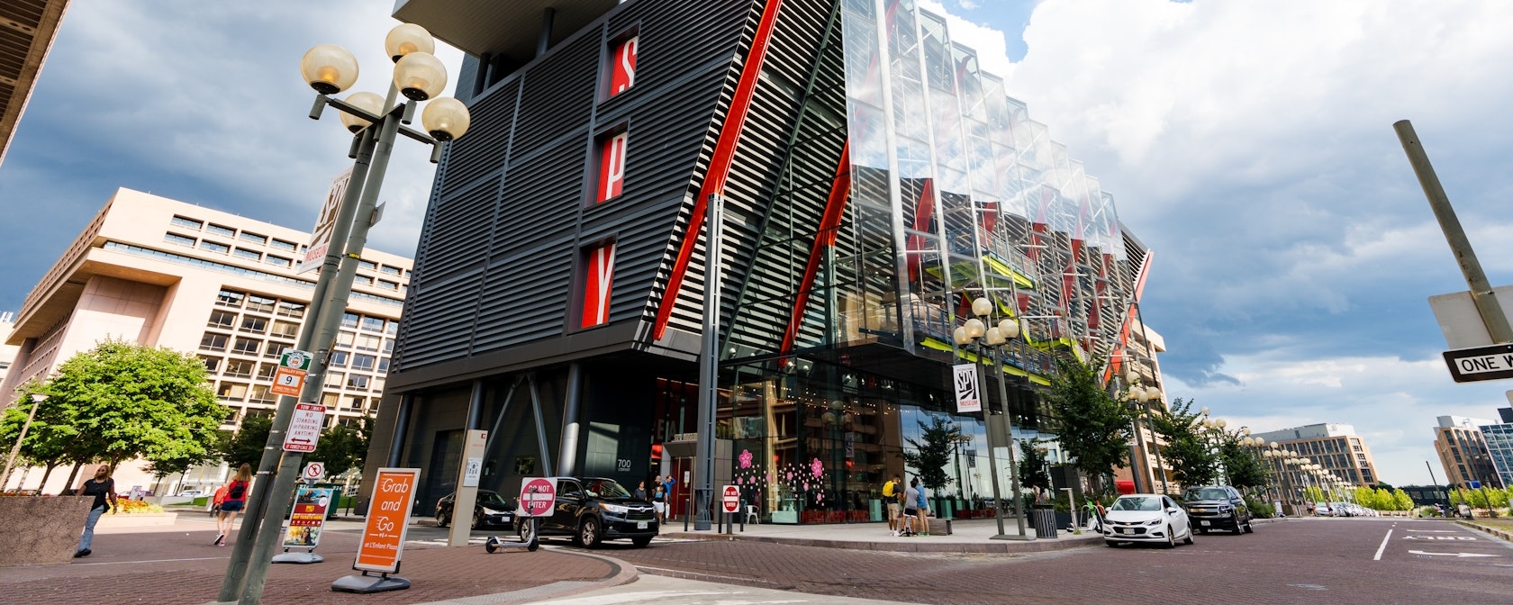 The modern glass and steel exterior of the International Spy Museum in Washington, DC, featuring red architectural accents and pedestrians along the street.
