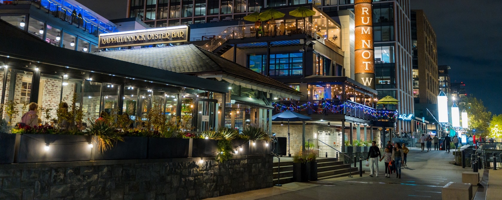Businesses are lit up and busy at night along The Wharf in DC.