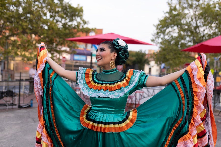 A folklórico dancer in a green traditional dress holds her skirt wide during an outdoor cultural performance in Washington, DC.