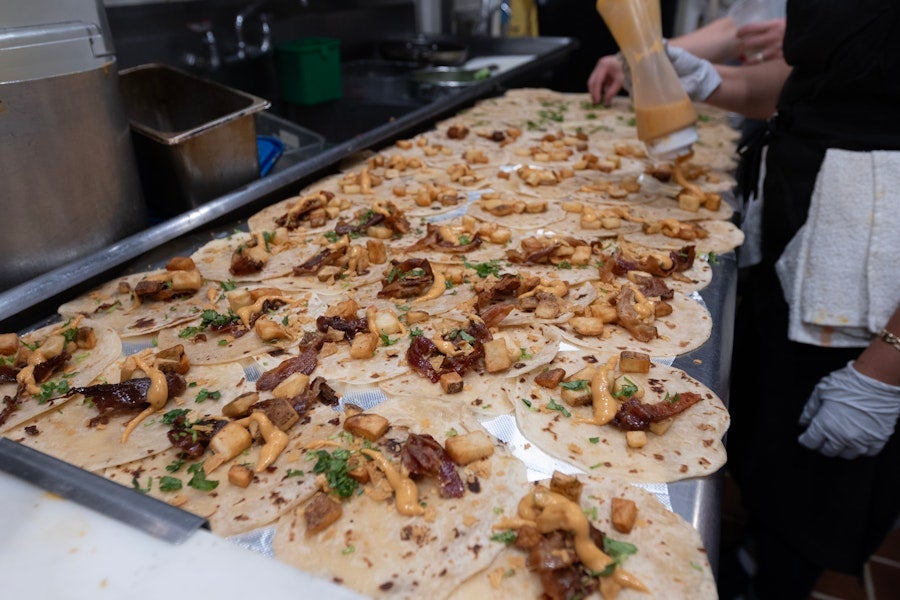 Fresh breakfast tacos are assembled on a prep line at La Tejana in Washington, DC, with tortillas topped with potatoes, meat, herbs, and sauce.