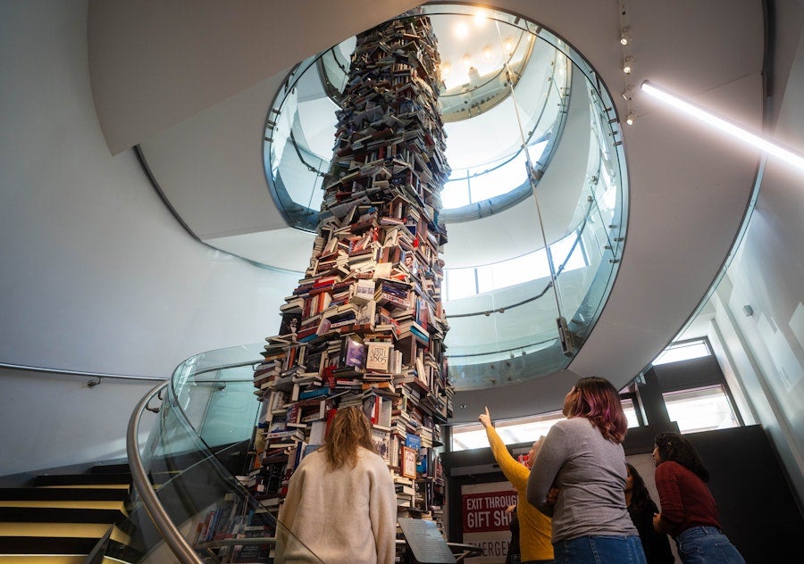 A group of people looks up at a soaring art installation of books, ascending within a staircase.