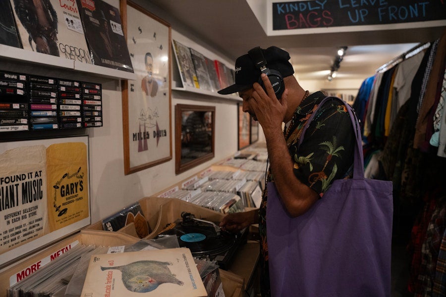Person listens to a vinyl record with headphones inside a cozy record shop.