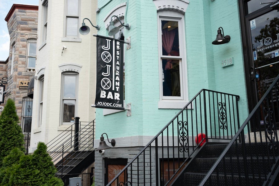 Pastel rowhouse exterior with stairs leading up to the JoJo Bar restaurant entrance.