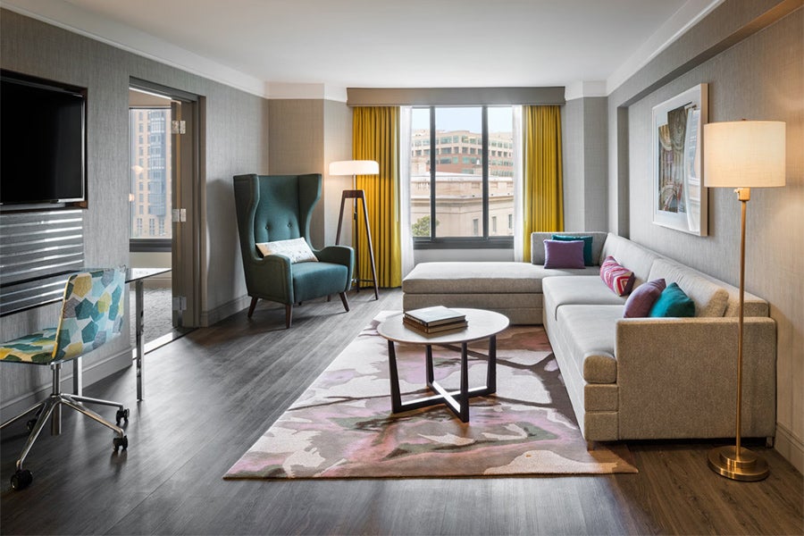 Spacious guest room at The Darcy Hotel in Washington, DC with modern furnishings, large windows, seating area and city views