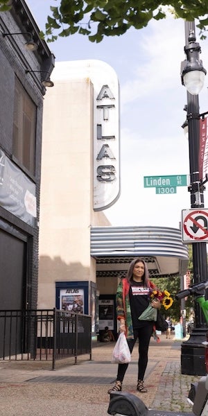 A person carries shopping bags while walking past the Atlas Theater on a city sidewalk.